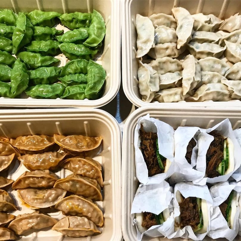 Four takeout containers filled with green, white, and brown dumplings, and bao buns.