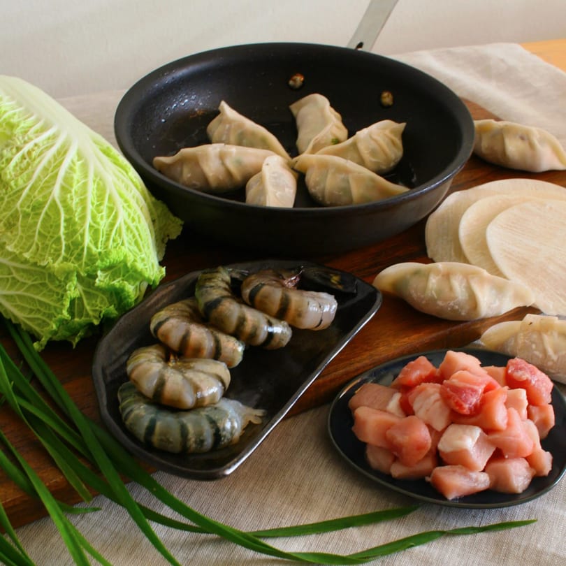 Dumpling ingredients including cabbage, shrimp, pork, wrappers, and cooked dumplings in a pan.