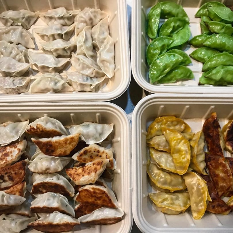 Four containers filled with various dumplings: steamed, pan-fried, green, and yellow.